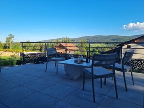 Un patio al aire libre con una mesa y sillas, vista a una montaña y un edificio en el fondo.