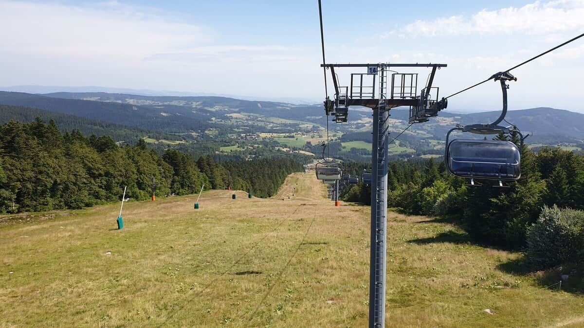 Eine Seilbahn mit freiem Blick auf die umliegende Landschaft, darunter ferne Hügel und ein bewaldetes Gebiet.