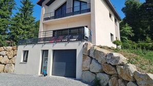 A two-story modern house with a stone facade, a garage, and a balcony with a metal railing. - Le Perchoir de l'Olme (Chalmazel-Jeansagniere)