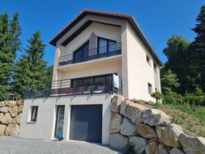 Una casa moderna de dos pisos con fachada de piedra, garaje y balcón con barandilla metálica.