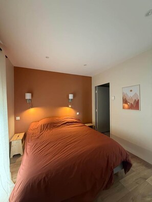 Un dormitorio con una cama, dos lámparas de noche, una puerta y un cuadro colgado en la pared.