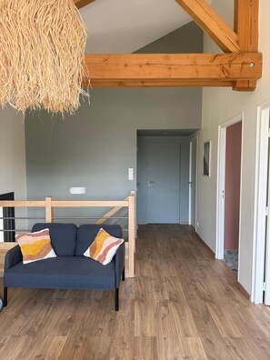 Una habitación con techo de madera, un sofá con cojines, una lámpara colgante y una puerta al fondo.