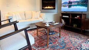 Una sala de estar con sofá, mesa de centro, chimenea, televisor y estantería.