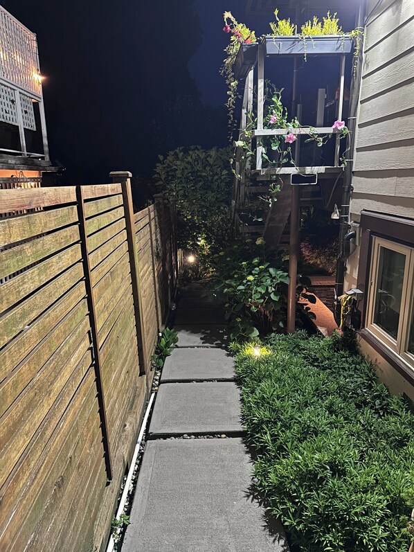 A narrow pathway leading to a wooden fence and a building with a window.