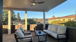 Un patio techado al aire libre con ventilador de techo, un sofá, dos sillones y una mesita.