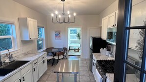 Una cocina moderna con armarios blancos, una isla central, un comedor y vistas a un dormitorio.