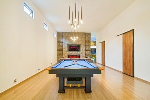 Una mesa de billar en una habitación moderna con chimenea, un cartel de Netflix y una puerta de madera.