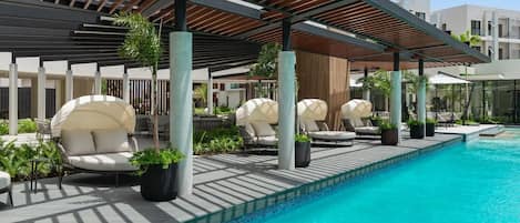 A modern pool area with lounge chairs and umbrellas, surrounded by potted plants and a covered seating area.