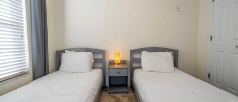 Habitación doble con dos camas, una mesita de noche con lámpara y una ventana con persianas.