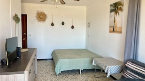 A bedroom with a bed, a desk with a computer, a ceiling fan, and a small table with a tablecloth.