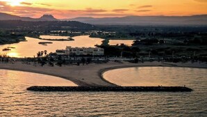A coastal landscape with a river, buildings, and a mountain in the background during sunset.