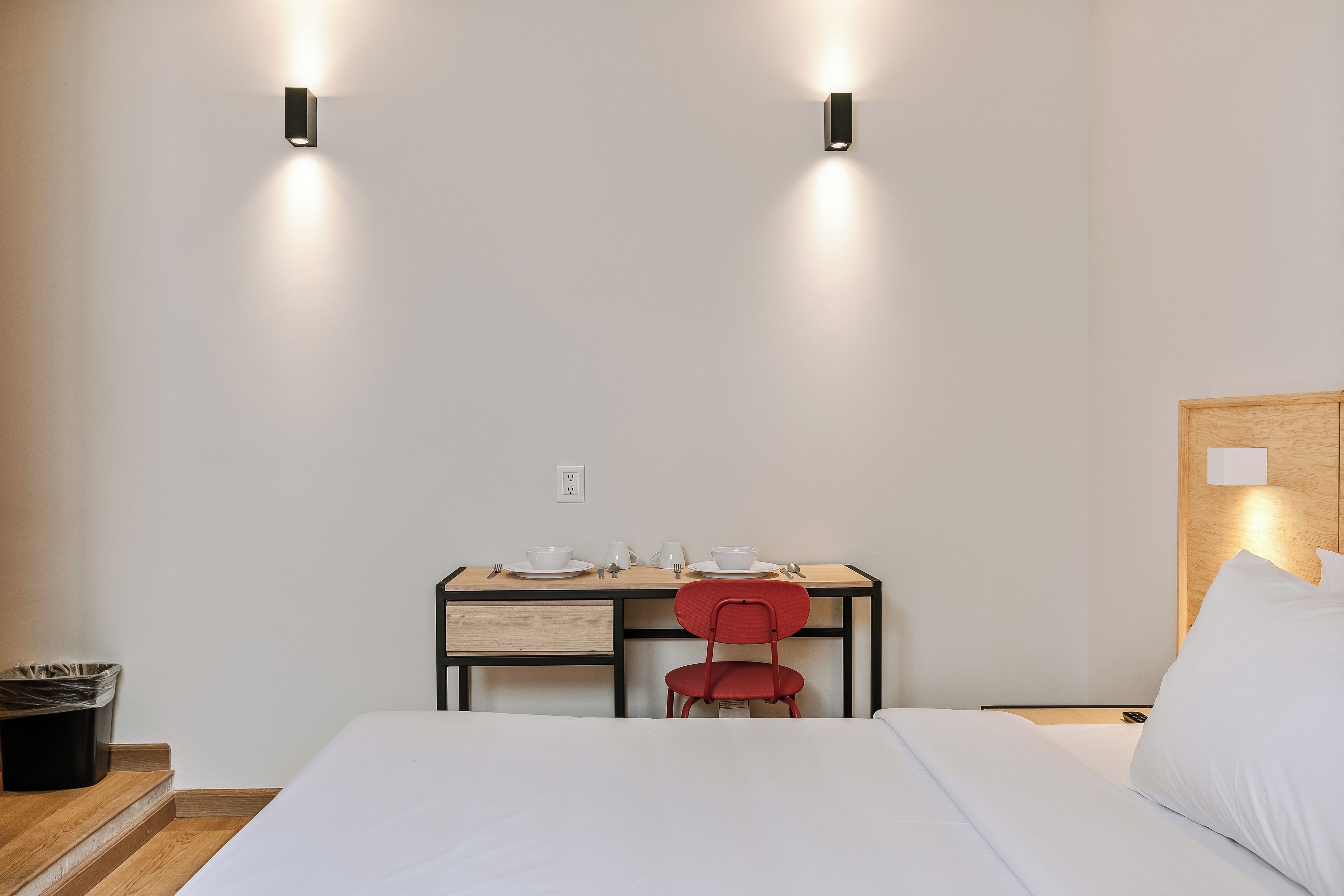 Habitació d'hotel amb un llit, una taula de treball amb cadira i dues làmpades murals.