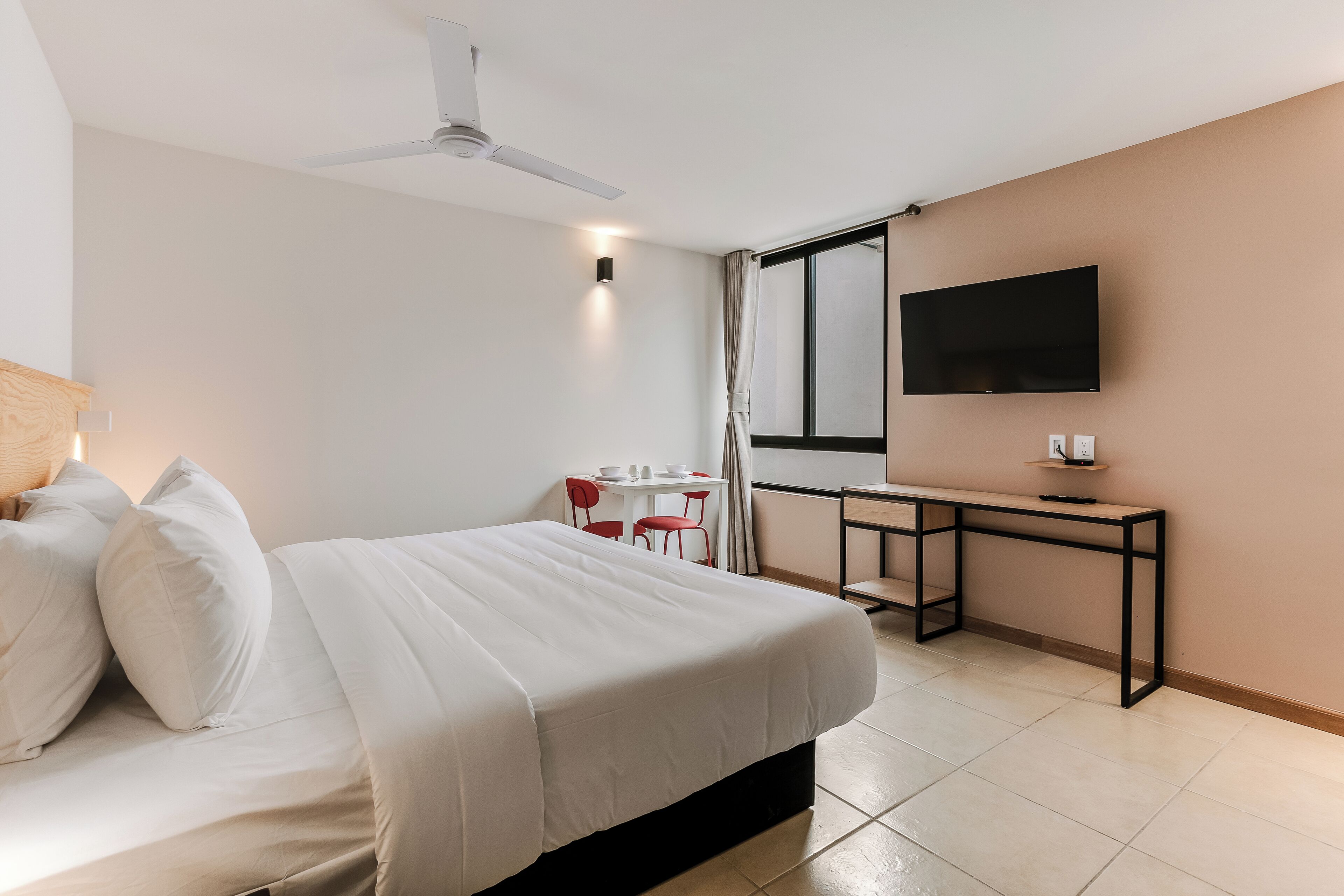 A hotel room with a bed, a desk, a chair, a TV, and a ceiling fan.