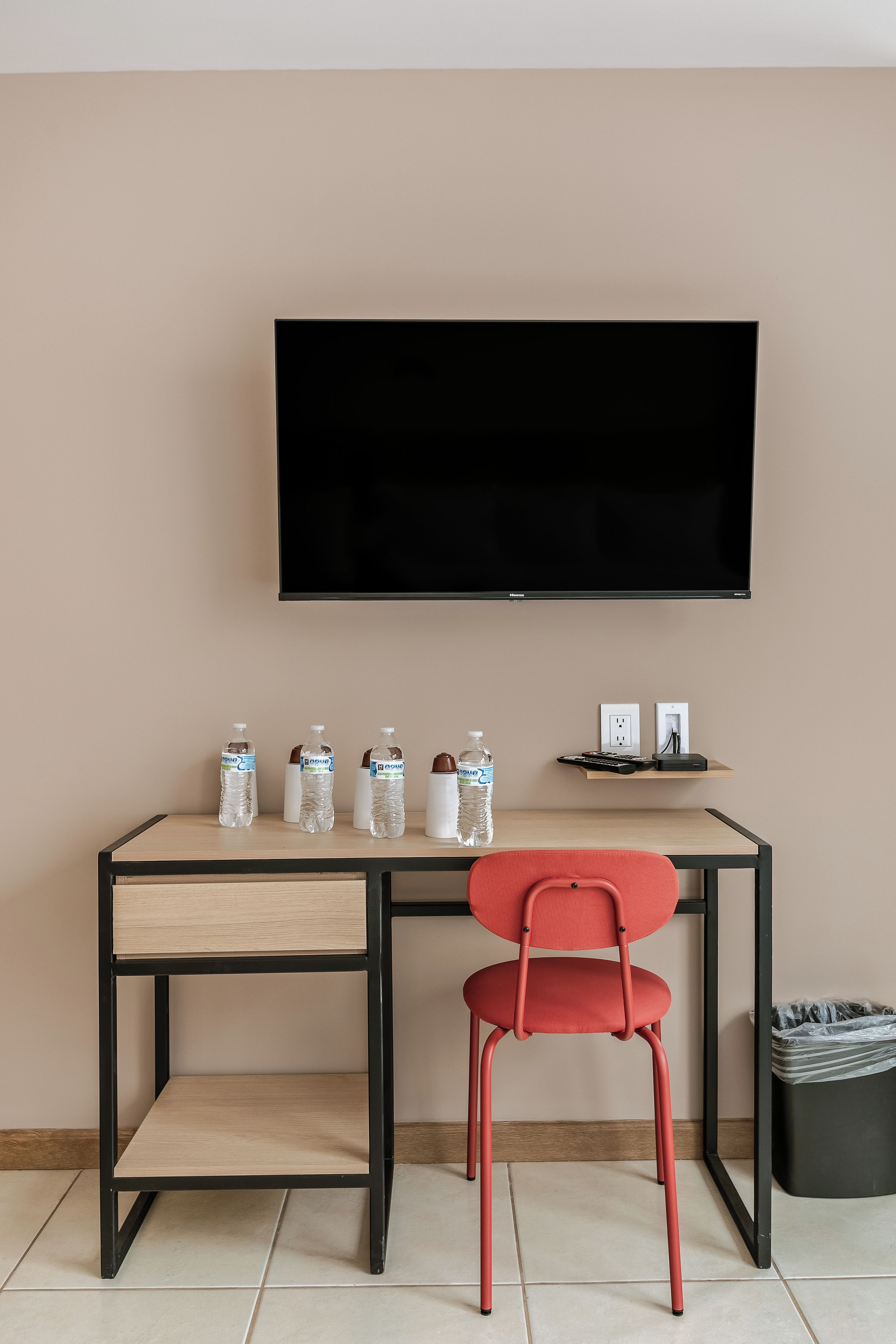 Una habitación moderna con una televisión de pantalla plana montada en la pared, un escritorio de madera con una silla y un cesto de basura.