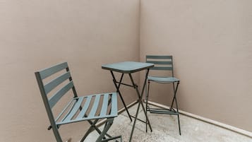 Ein kleiner Sitzbereich im Freien mit zwei Metallstühlen und einem Tisch, vor einer Wand mit strukturierter Oberfläche und geneigter Decke.
