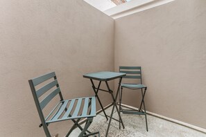 A small outdoor seating area with two metal chairs and a table, set against a textured wall with a sloped ceiling.