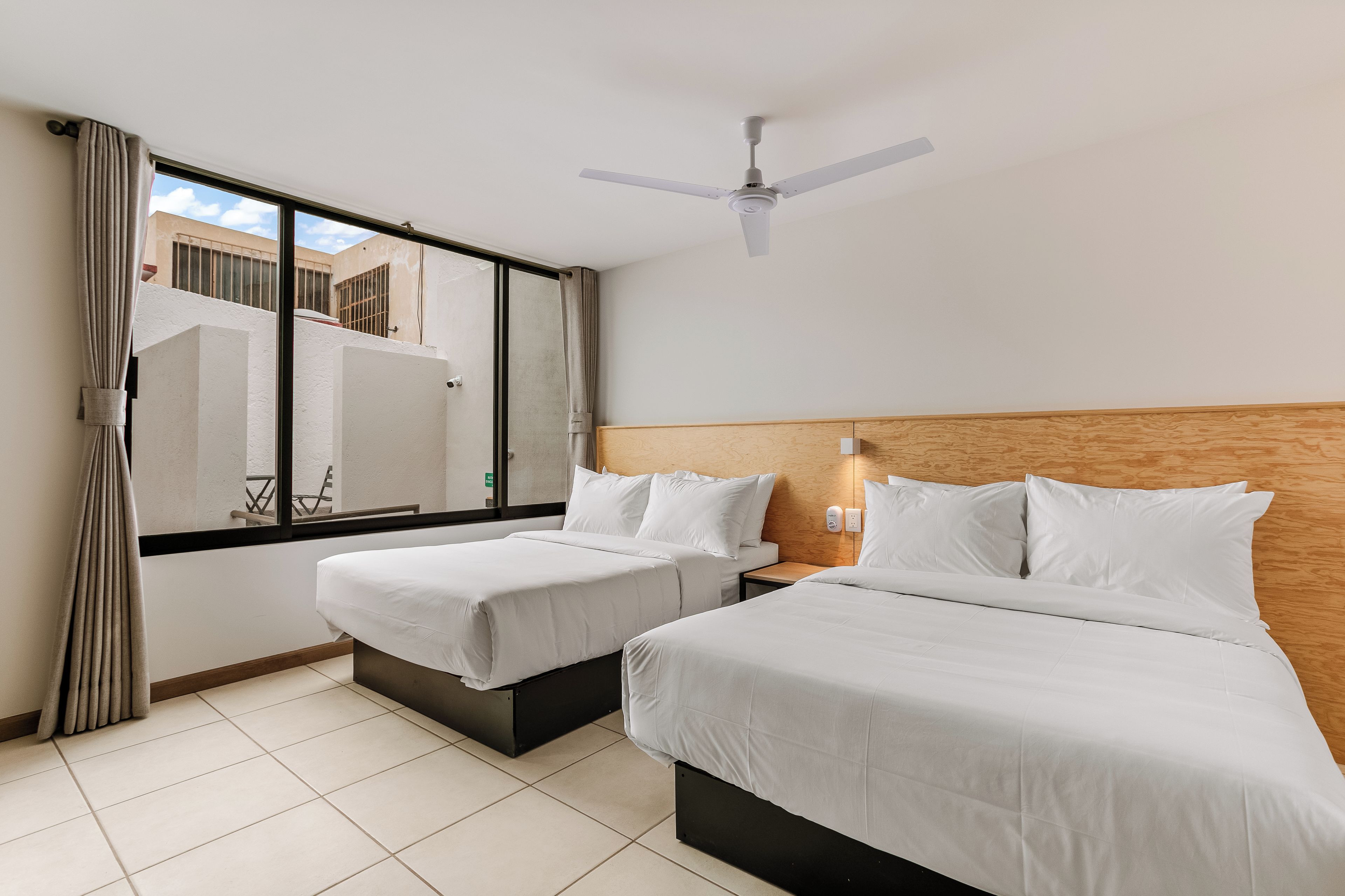 A hotel room with two beds, a ceiling fan, and a view of the outside.