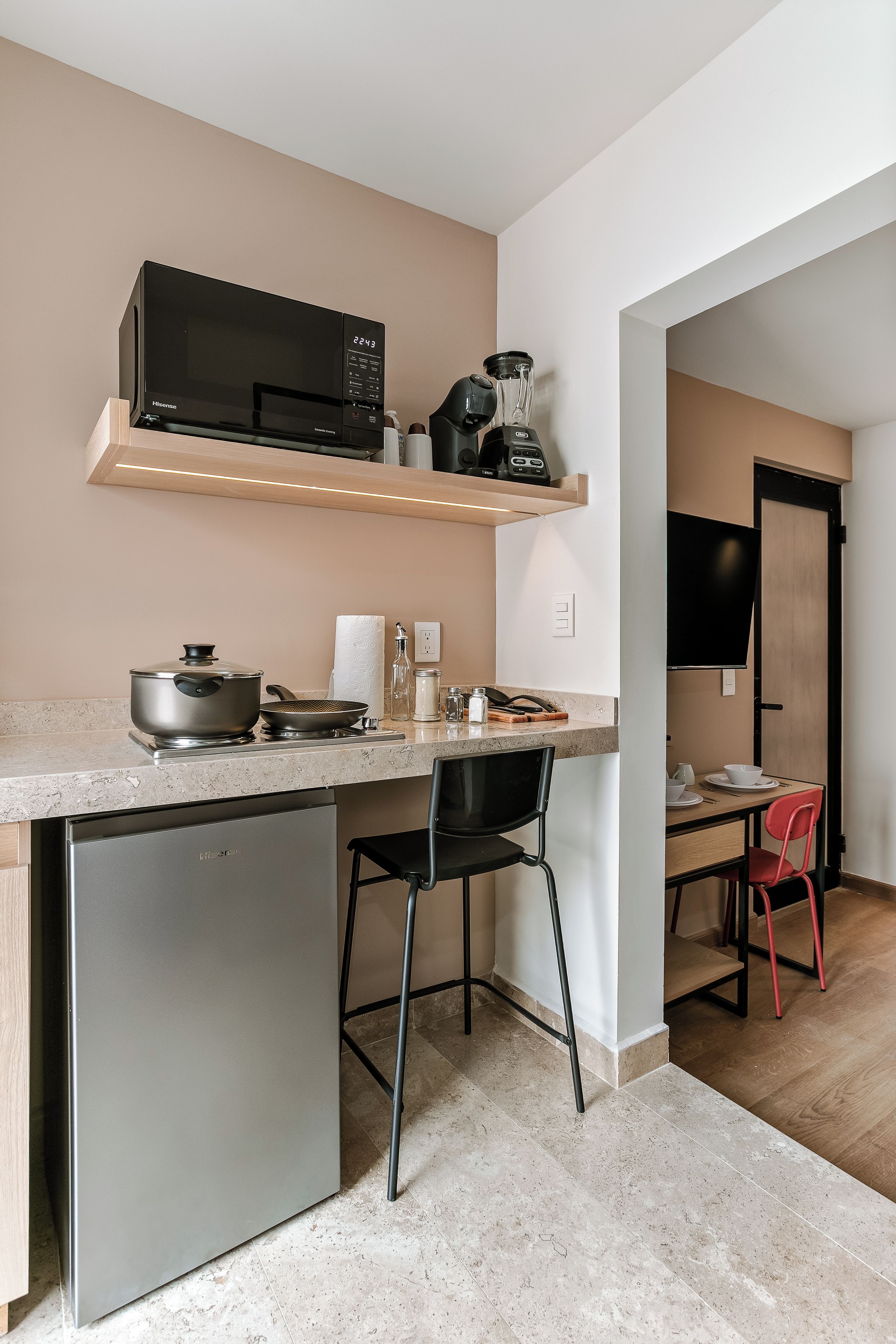 Eine kompakte Küche mit Mikrowelle, Mixer und kleinem Kühlschrank.