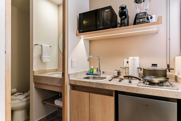 A modern kitchen with a built-in microwave, coffee maker, and blender on a shelf, a sink with a faucet, and a stove with a frying pan. - Pájaros by Homirent (Queretaro)