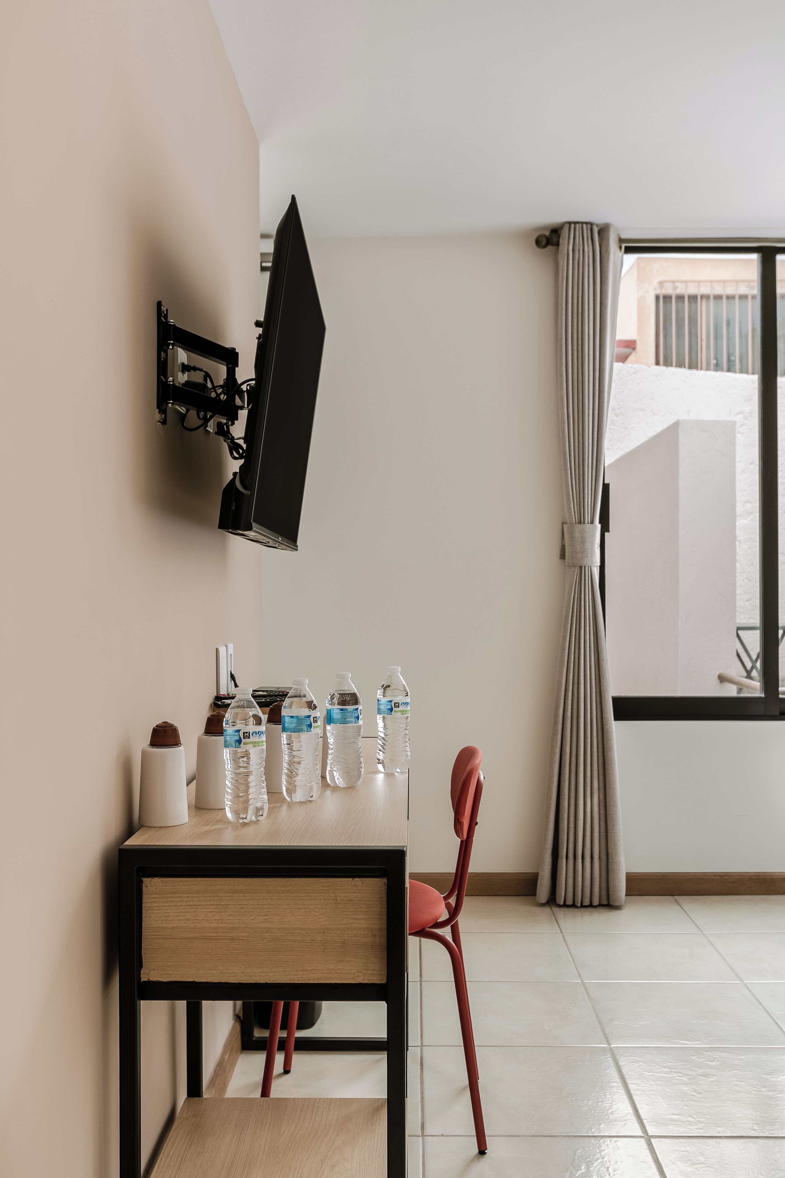 Una habitación con una mesa de comedor, sillas, televisor montado y una ventana con cortinas.