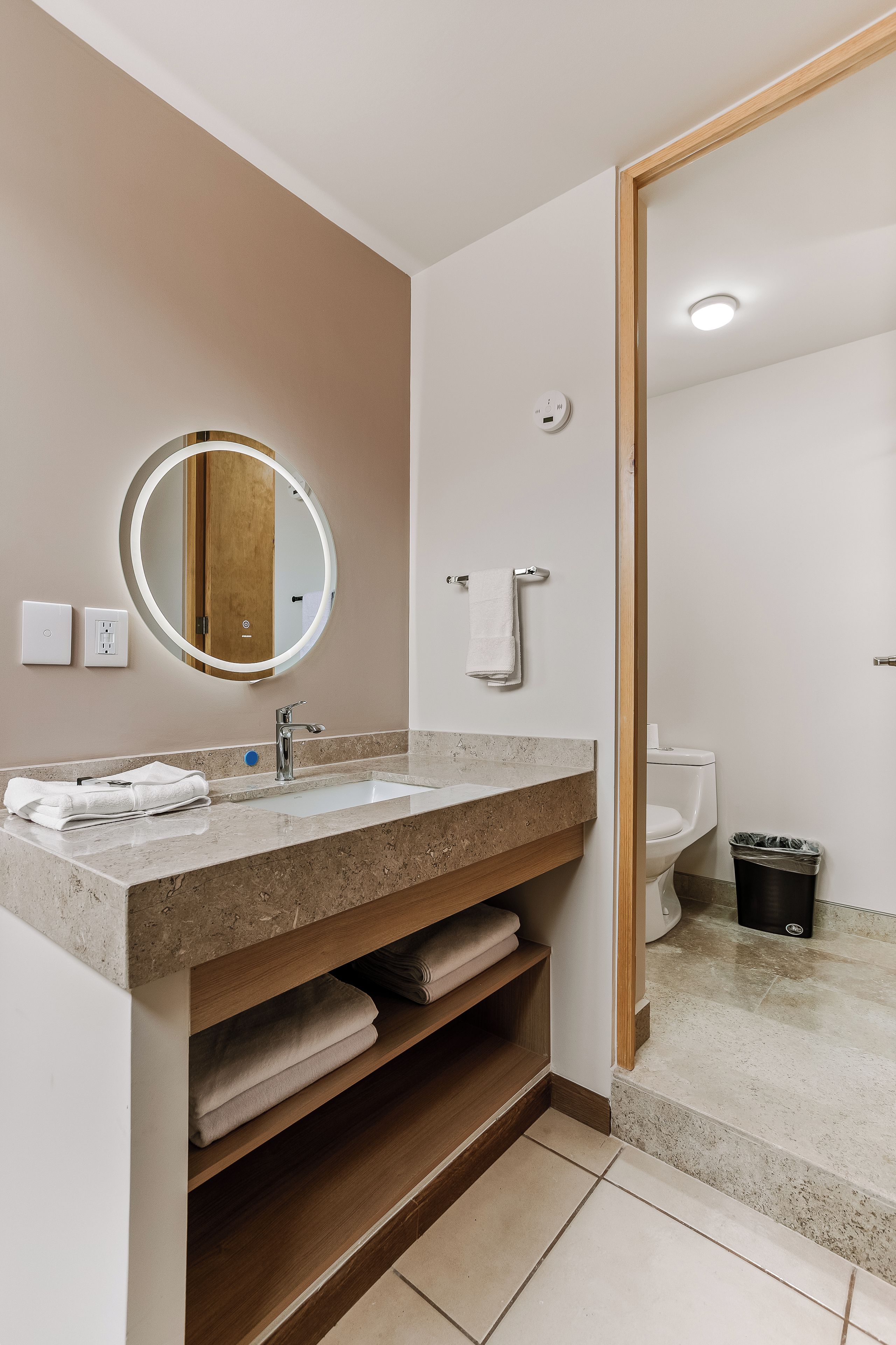 Un baño moderno con tocador, lavamanos, espejo, toallero y retrete.