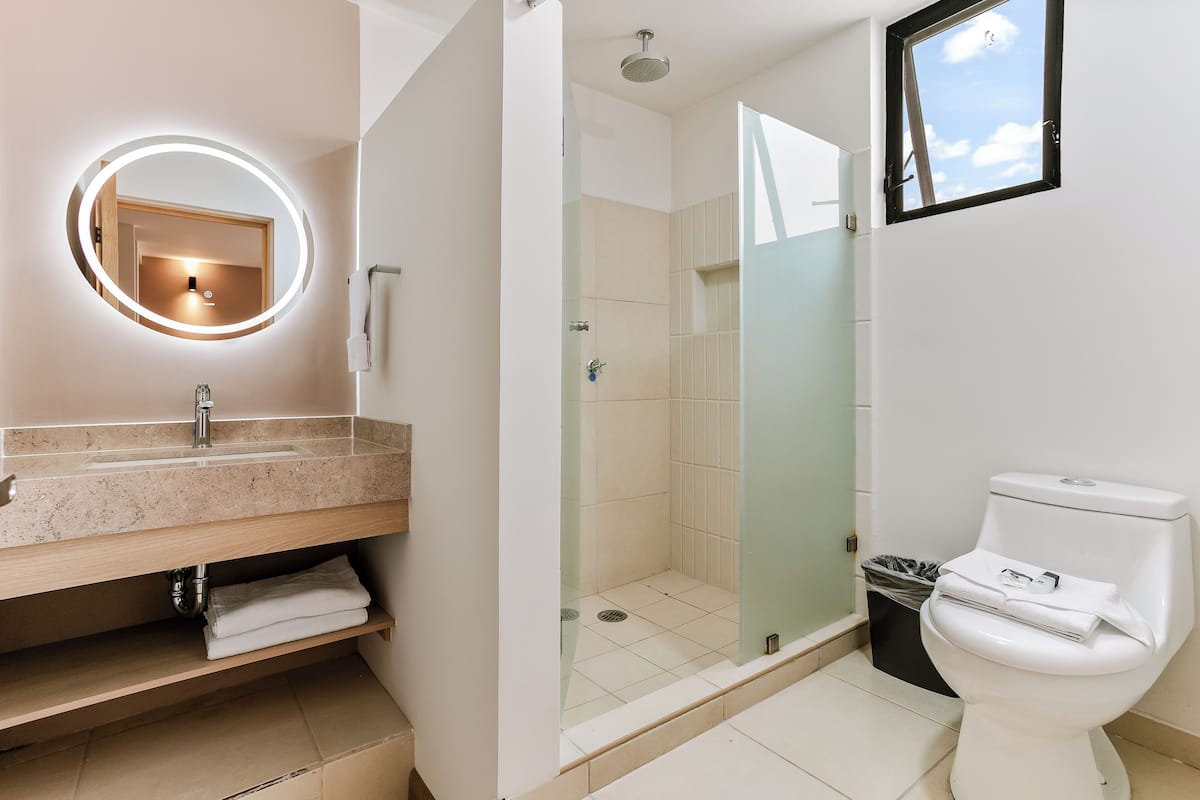 A modern bathroom with a round mirror, a sink, a toilet, and a glass-enclosed shower.