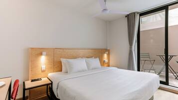 Habitación de hotel con una cama grande, un escritorio con una silla, un ventilador de techo y vistas al exterior.