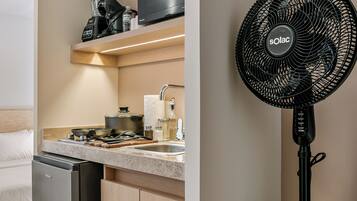 A modern kitchen with a built-in refrigerator, a stove, and a sink. There is a black fan on the right side of the image.