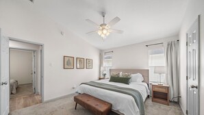 A bedroom with a bed, a bench, a nightstand, a ceiling fan, and framed pictures on the wall. - Charming 3-bedroom house with fast WiFi and AC in fabulous Spring (Spring)