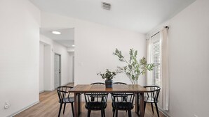 A dining area with a wooden table and black chairs, a potted plant, and a window with blinds. - Charming 3-bedroom house with fast WiFi and AC in fabulous Spring (Spring)