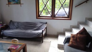 Een kamer met een bank, een kleintje tafeltje met een speeltje, een raam met uitzicht op bomen, en een trap.