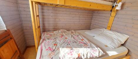 A bunk bed with a floral bedspread and pillows, wooden walls, and a small wooden chair.
