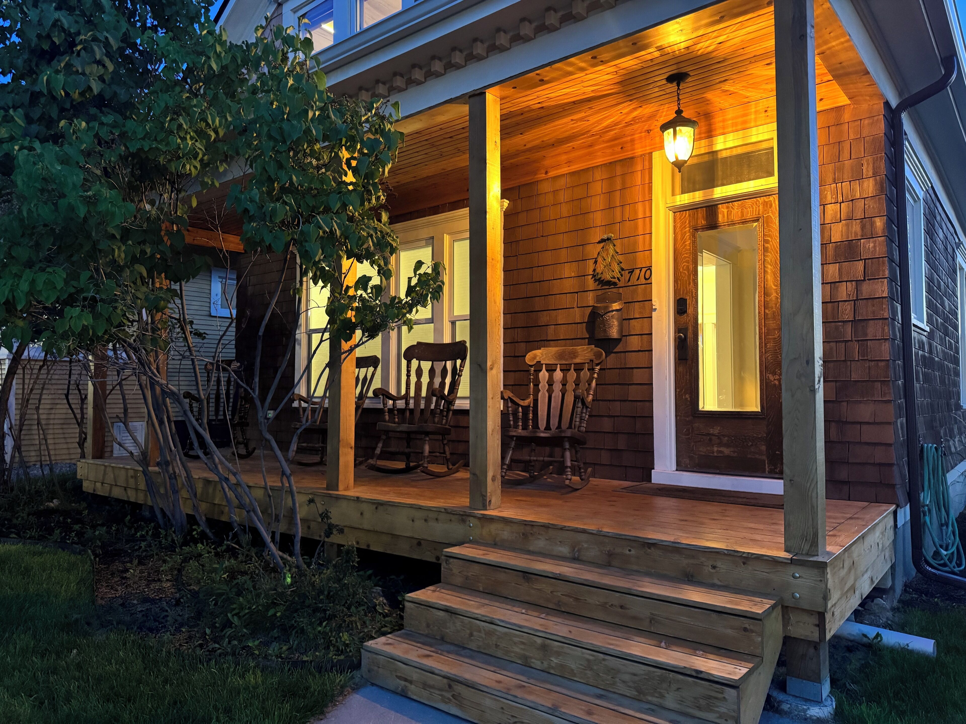 A wooden porch with a bench and chairs, a door with a number, and a hanging light fixture.