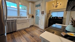 A kitchen with white cabinets, a stainless steel refrigerator, a wooden floor, and a glass door leading to another room. - Charming Vintage Retreat in the Heart of Anaconda. (Anaconda)