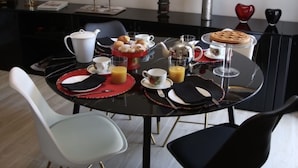 A dining area with a black table set for breakfast, including croissants, orange juice, and coffee. There are two framed pictures on the wall, a vase with flowers, and a flat-screen TV mounted above the table. - Calefati Gallery Luxury Apartment  (Bari)