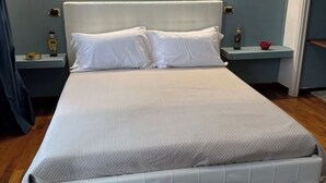 A neatly made bed with white linens and a light-colored headboard in a modern room with a wooden floor and a blue accent wall. - Calefati Gallery Luxury Apartment  (Bari)