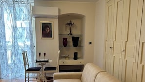 A living room with a beige sofa, a small table with two chairs, a chandelier, and a painting on the wall. - Calefati Gallery Luxury Apartment  (Bari)