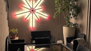 A patio area with a glass table and chairs, a large potted plant, and decorative light installations on the wall. - Calefati Gallery Luxury Apartment  (Bari)
