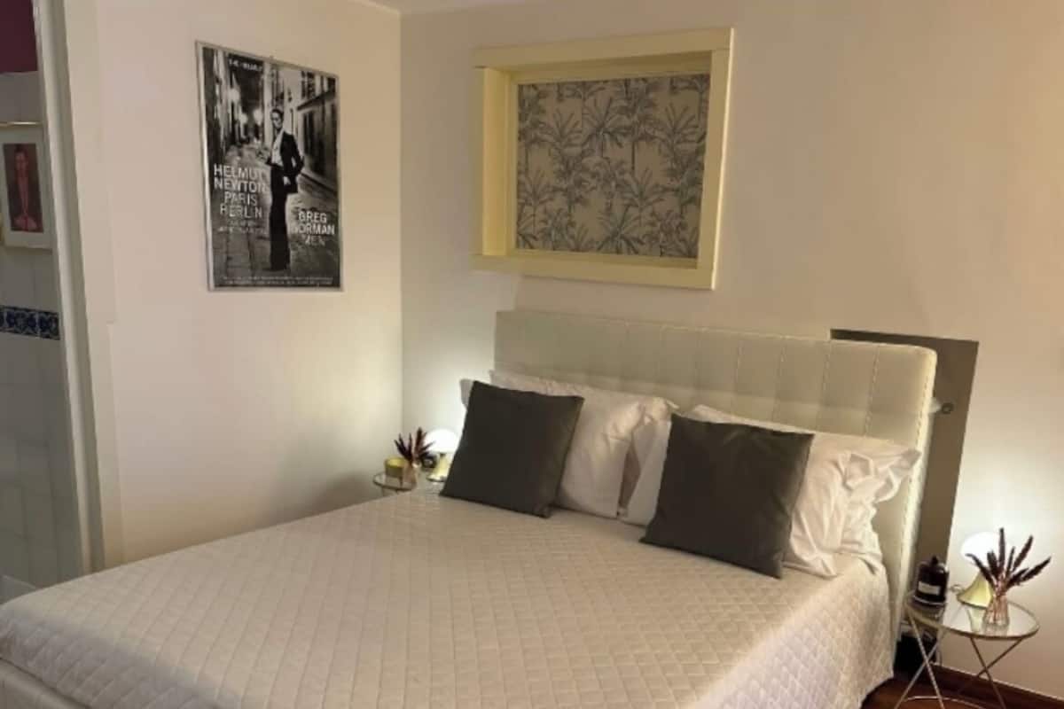 Ein ordentlich bezogenes Bett mit einer gesteppten Decke, ein Kopfteil mit einem hellen Paneel und ein Poster an der Wand.