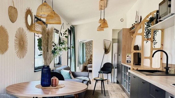 Una cucina moderna con mobili scuri, un piano di lavoro in legno e un rubinetto nero. È presente una zona pranzo con un tavolo e sedie rotonde.