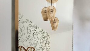 Camera da letto con testiera in rattan, letto con biancheria bianca e lampadario pendente in rattan.
