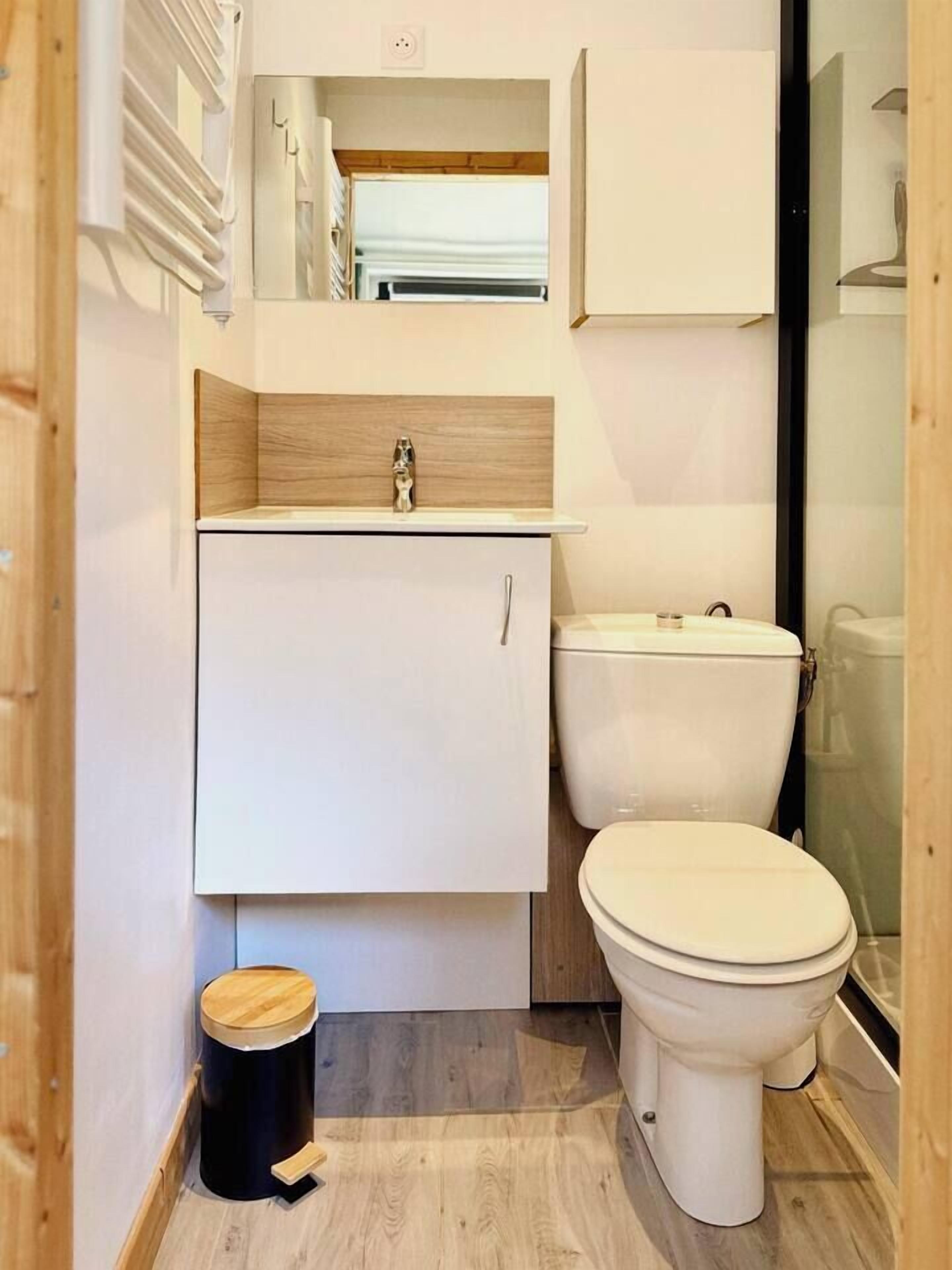 Une petite salle de bain avec des toilettes blanches, un petit meuble et un plancher en bois.