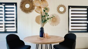 Un tavolo rotondo in legno con due sedie nere, circondato da decorazioni murali a forma di raggi di sole e un vaso con piante verdi.