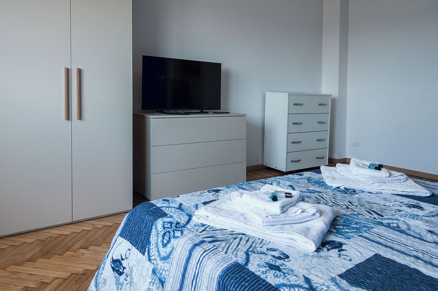A bedroom with a bed, a wardrobe, a TV, and a dresser.
