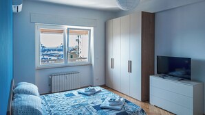 Een slaapkamer met een bed, een televisie, een kledingkast en een raam met uitzicht op een haven.