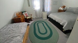Un dormitorio con dos camas, un aparador de madera, una silla, un radiador y una ventana con cortinas.