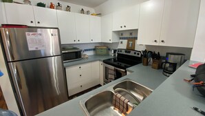Una cocina compacta con armarios blancos, un refrigerador de acero inoxidable, un microondas, un horno y una cafetera.