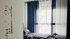 A bedroom with two beds, a window with curtains, a wall-mounted light switch, and a door. - Very nice apartment for rent in kenitra with swimming pool and gym (Kénitra)