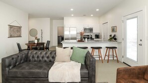 Ein modernes Wohnzimmer mit einem dunkelgrauen Ledersofa, einem Esstisch mit Stühlen und einer Küchenzeile mit Kochinsel.