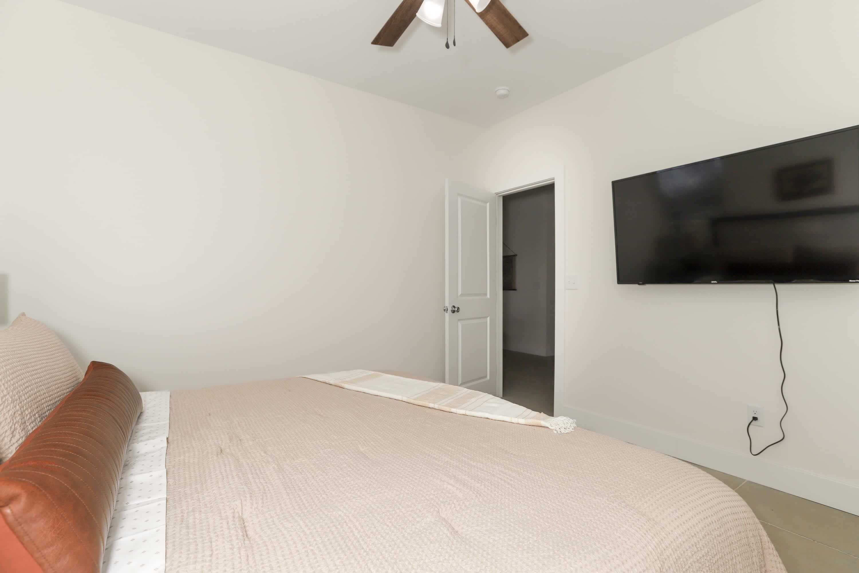 Un dormitorio con cama, televisor montado en la pared y una puerta que da a otra habitación.